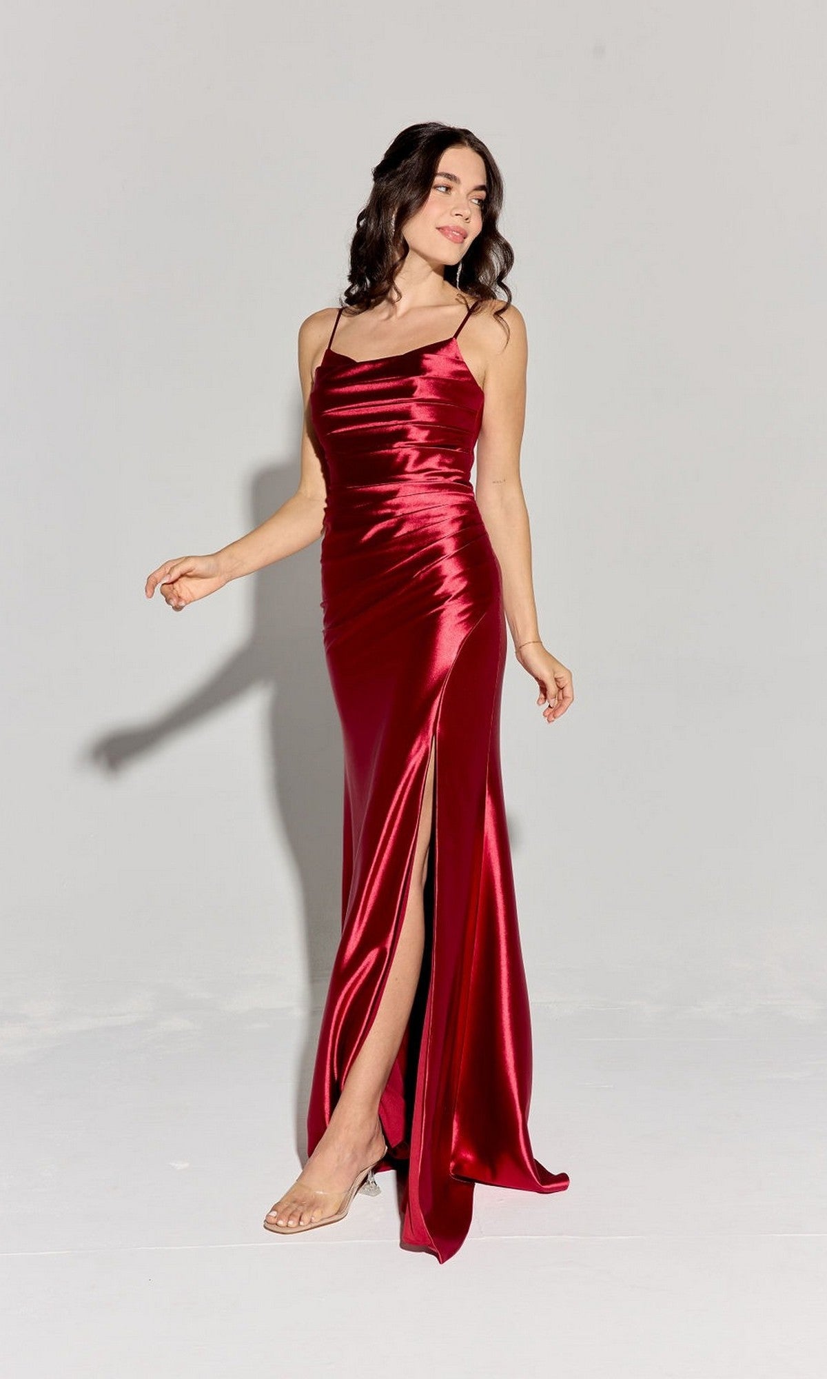 A woman models the Eureka EK108 long prom dress—shiny red stretch satin, spaghetti straps, and a thigh-high slit—against a plain light background.